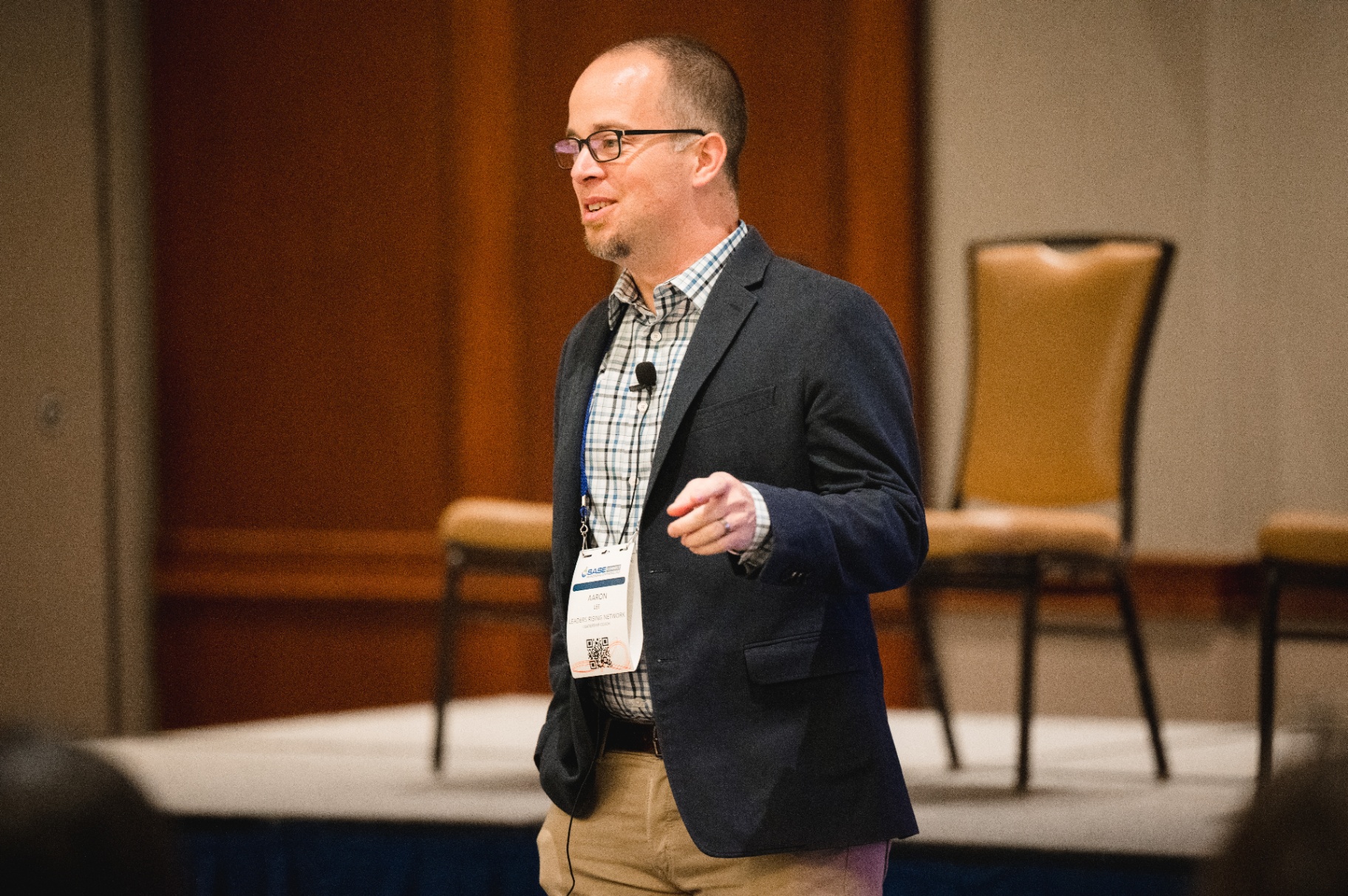 Aaron Lee speaking at the SASE conference in a navy blazer, mid-gesture
